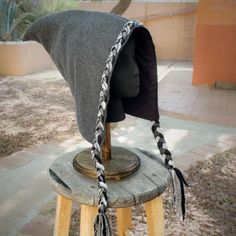 a gray hat with braids on top of a wooden stool next to a tree