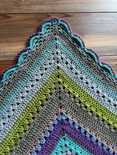 a multicolored crocheted blanket laying on top of a wooden floor