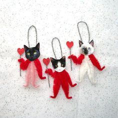 three cat keychains are hanging on a white sheet with red and white hearts