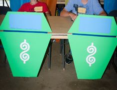 two people sitting at a table with green and blue boxes on it that have dollar signs painted on them