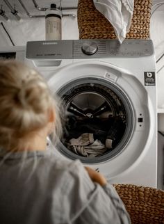 a woman is looking at the front loader of a washing machine in a laundry room