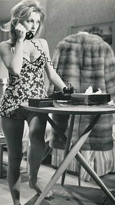 a woman is talking on the phone while sitting at a table with a cake in front of her