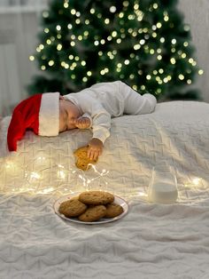 a little boy laying on top of a bed next to a plate of cookies and milk