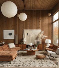 a living room filled with lots of furniture next to large windows and wooden paneled walls