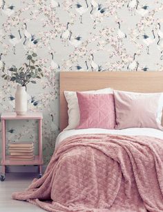 a bed with pink sheets and pillows in front of a floral wallpaper