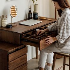 a woman sitting at a wooden desk with drawers in front of her and looking into the drawer