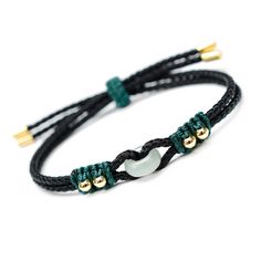 a black cord bracelet with two gold beads and green cords on the end of it