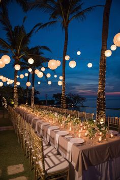 a long table with paper lanterns hanging from it's ceiling and lit candles on the tables