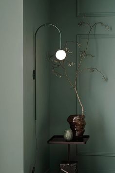 a room with green walls and a plant in the corner on a shelf next to a lamp