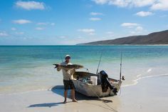 a man standing next to a boat on top of a sandy beach near the ocean