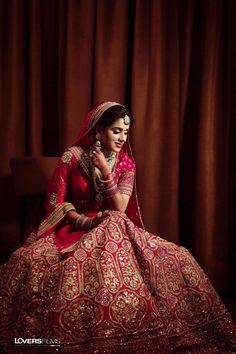 a woman in a red and gold bridal gown sitting on a chair with her hands to her face