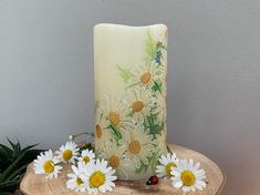 a candle with daisies and ladybugs on it sitting on a tree stump