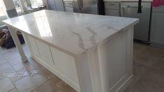 a white kitchen island with marble top in the middle of a tile flooring area