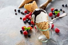 an ice cream cone with chocolate and raspberries on the side, surrounded by berries