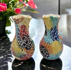 two colorful vases sitting on top of a table next to each other with flowers in the background