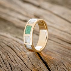 a gold ring with green and white stone inlays sits on a piece of wood