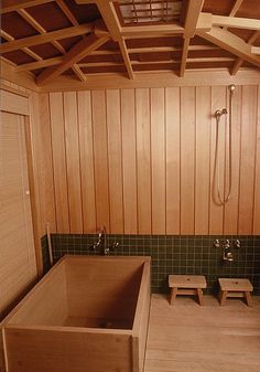 a large wooden bathtub sitting inside of a bathroom next to two stools and a shower