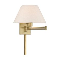 a wall light with a white shade on the top and one arm in brass finish