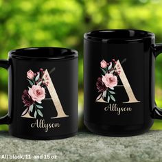 two black coffee mugs with floral designs on them, one has the letter a