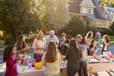 a group of people standing around a table with food on it in front of a house