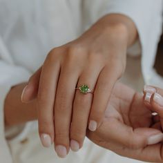 two people holding each other's hands with a green ring on their finger,