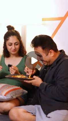 two people sitting on a bed eating pizza and talking to each other while the man is holding a plate