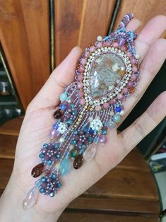 a hand holding a beaded brooch with beads and stones in it's center