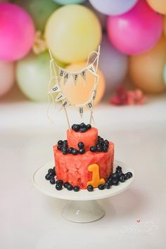 a birthday cake with blueberries and blackberries on top is displayed in front of balloons