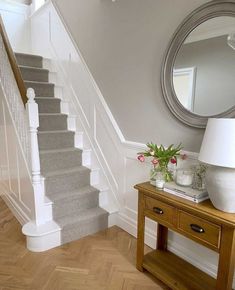 there is a vase with flowers sitting on the table next to the stairs and mirror