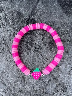 a pink and green beaded bracelet with a strawberry on the end, sitting on a rock