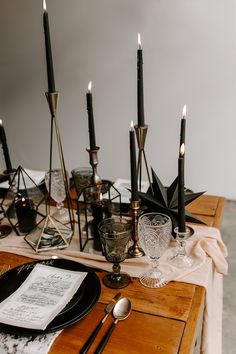 a wooden table topped with black candles and plates covered in napkins next to wine glasses