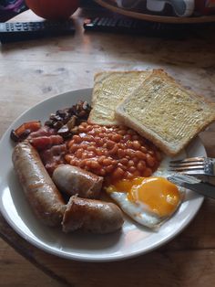 a white plate topped with eggs, beans and toast on top of a wooden table