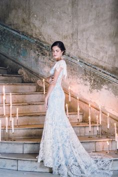 a woman in a wedding dress standing on some stairs with candles behind her and looking off into the distance