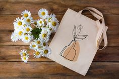 a tote bag with daisies in front of it on a wooden table next to flowers