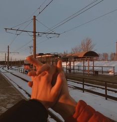 a person holding their hand up in front of a train track with snow on the ground