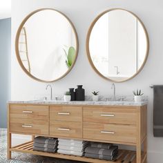 two round mirrors are above the double sink vanity in this modern bathroom with wood cabinets and marble countertops