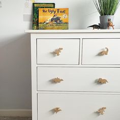 a white chest of drawers with an elephant book and toy dinosaurs on top of it