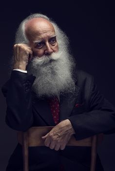 an old man with a long white beard sitting in a chair and looking at the camera