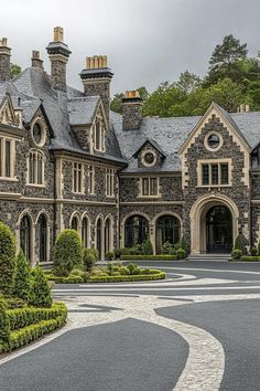 a large stone house surrounded by lush green trees and shrubbery on a cloudy day