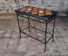 a small table with an orange and black mosaic design on it's top sitting in front of a brick wall