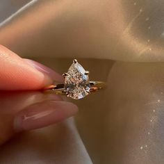 a woman's hand holding an engagement ring with a pear shaped diamond on it