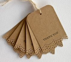 four tags with thank you written on them are hanging from twine string and placed on a white tablecloth