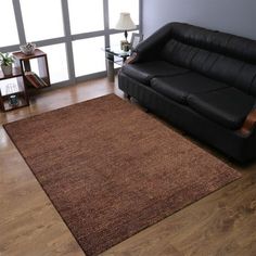 a living room with a black leather couch and wooden flooring next to a large window