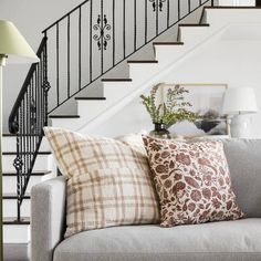 a living room filled with furniture and a stair case next to a white couch covered in pillows