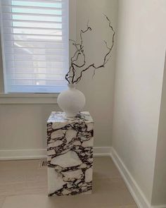 a white vase sitting on top of a marble block in front of a window with blinds