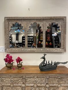 an ornate mirror hangs above a dresser with vases and flowers