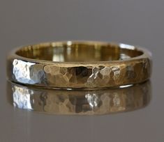 a close up of a gold wedding ring on a reflective surface with reflection in the background