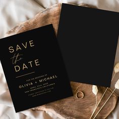 two black and gold save the date cards on top of a wooden tray with dried flowers