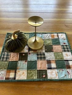 a quilted placemat with a gold candle holder on it and a green pumpkin