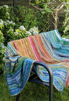 a multicolored crocheted blanket sitting on top of a chair in the grass